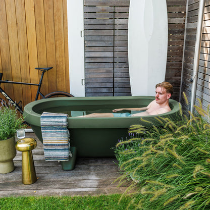 Man relaxing in an Olive Green Gardentub on a timber deck surrounded by plants